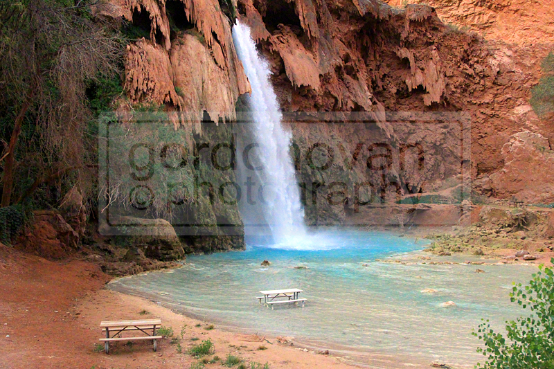The vibrant blue water contrasts against the striking red rocks of the canyon walls as Havasu Falls plunges nearly 100 feet into a wide pool of blue-green waters.