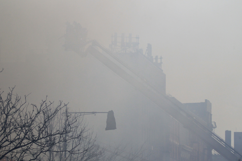 Through the smoke, New York City firefighters aboard a tower ladder prepare to hose down a building that collapsed on Park Ave. and 116th Street in New York City, March 12, 2014. (Gordon Donovan/Yahoo News)