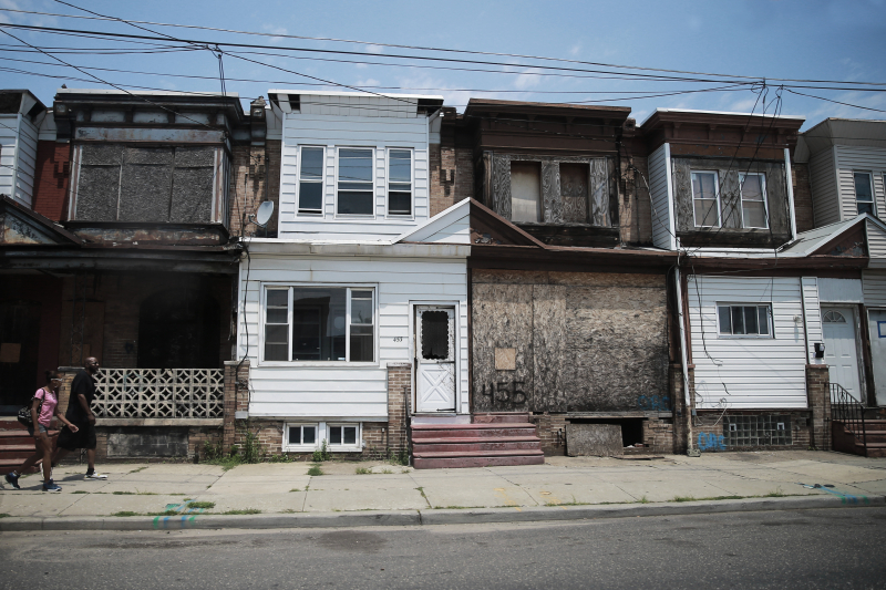 Two residents of Camden walk past a row homes, several of which are boarded up from neglect. (Gordon Donovan)
