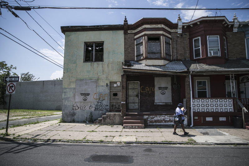 A postal worker walks their route past abandoned homes that were used by drug dealers in Camden N.J. (Gordon Donovan)