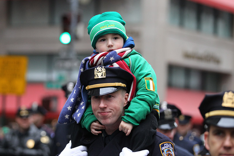 The son of a New York City Police officer get a ride as dad marches in the St. Patrick's Day parade past protesters, March 17, 2015, in New York. (Gordon Donovan)