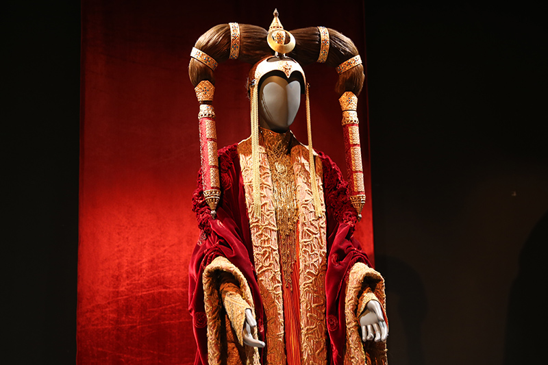 Amidala's Episode I Senate Gown is a bounty of luxurious fabrics. The loose-fitting robe was made in a velvet fabric decorated with bronze metallic, organza, enhanced with seed pearls on the collar and cuff facings. The underdress of silk taffeta was constructed using layers of pleated panels heavily decorated with antique beads. The Mongolian-inspired headdress was made in copper using an electro-forming technique and then gold plated. (Gordon Donovan/Yahoo News)