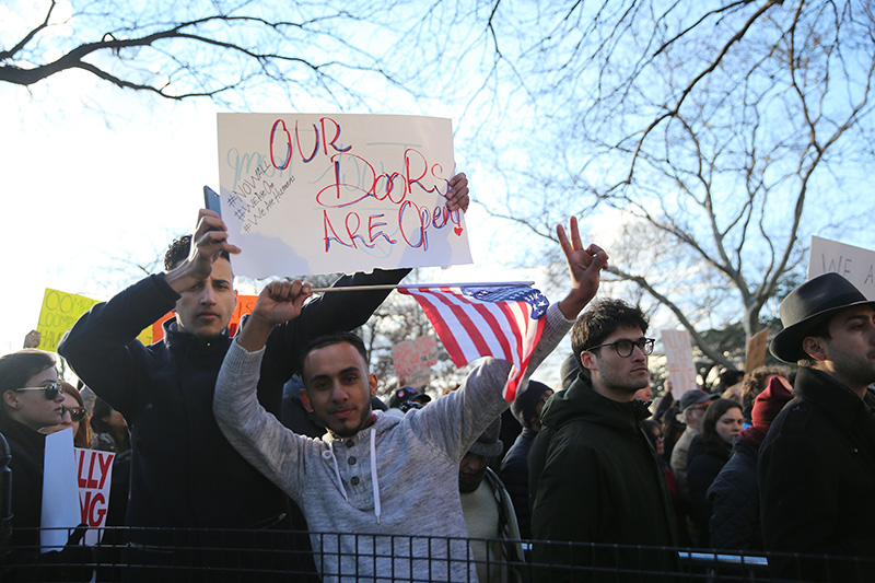 Two man wave flags and signs before a march in New York's Battery Park in New York, Jan. 29, 2017, protesting President Donald Trump's immigration order. (Gordon Donovan/Yahoo News)