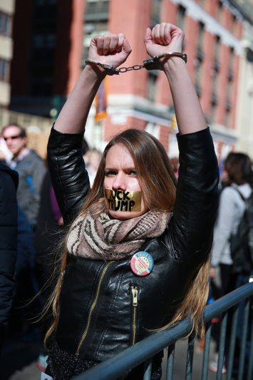 A young woman wears handcuffs and has her mouth taped shut with the words “F*** TRUMP” inside police barricades at the “Not My President’s Day” rally at Central Park West in New York City on Feb. 20, 2017. (Gordon Donovan/Yahoo News)